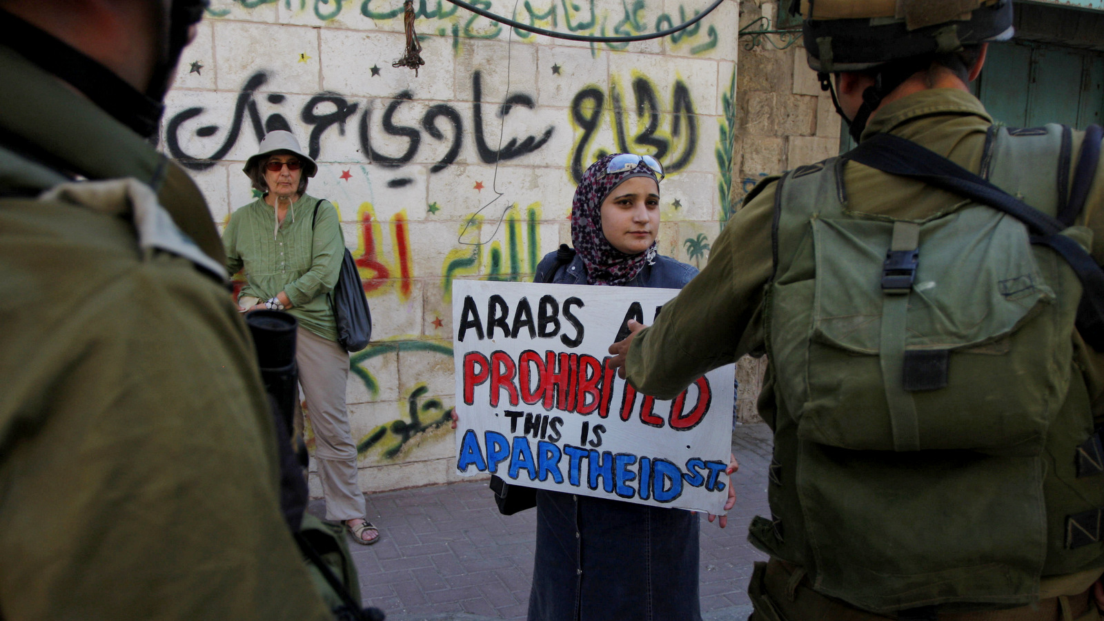 以色列士兵在2011年9月14日在希布伦关闭Al-Shuhada街的示威活动中，面对青年反定居组织的激进分子。墙上的阿拉伯涂鸦上写着：“ Hajj Shadi Arafat”。 （美联社/纳赛尔·史基）