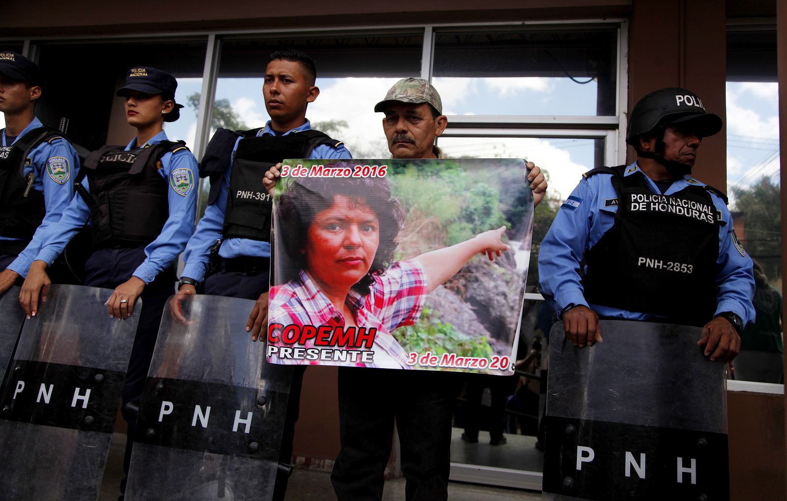 A man, flanked by police, holds a placard showing an image of slain environmental activist and Goldman Environmental Prize winner Berta Caceres, as part of a protest demanding justice for her murder, outside the Prosector's Office in Tegucigalpa, Honduras, March 2, 2018. (AP/Fernando Antonio)