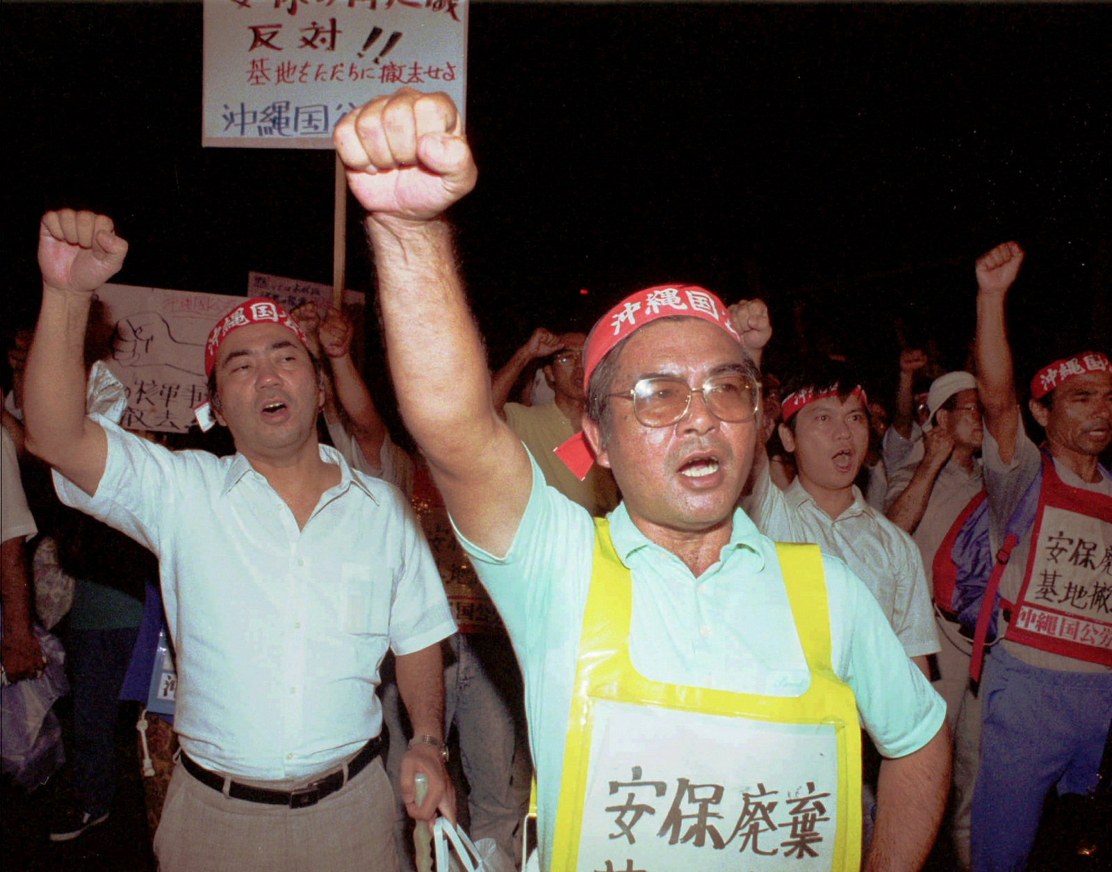 Workers clench their fists and shout slogans in front of the gate of Camp Foster, a U.S. Marine base, in Ginowan, northeast of Okinawa's largest city of Naha Tuesday evening, Sept. 26, 1995. Some 3,000 islanders held a rally and took the streets to protest the rape of an Okinawan schoolgirl by three U.S. servicemen. (AP/Koji Sasahara)