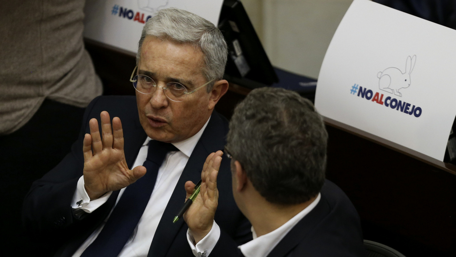 Former president and opposition Senator Alvaro Uribe talks with Senator Ivan Duque at his desk covered in signs that say in Spanish "No to the rabbit," a local way to refer to cheating, at the Senate in Bogota, Colombia, Nov. 24, 2016, the day the government and FARC signed a revised peace pact. (AP/Fernando Vergara)