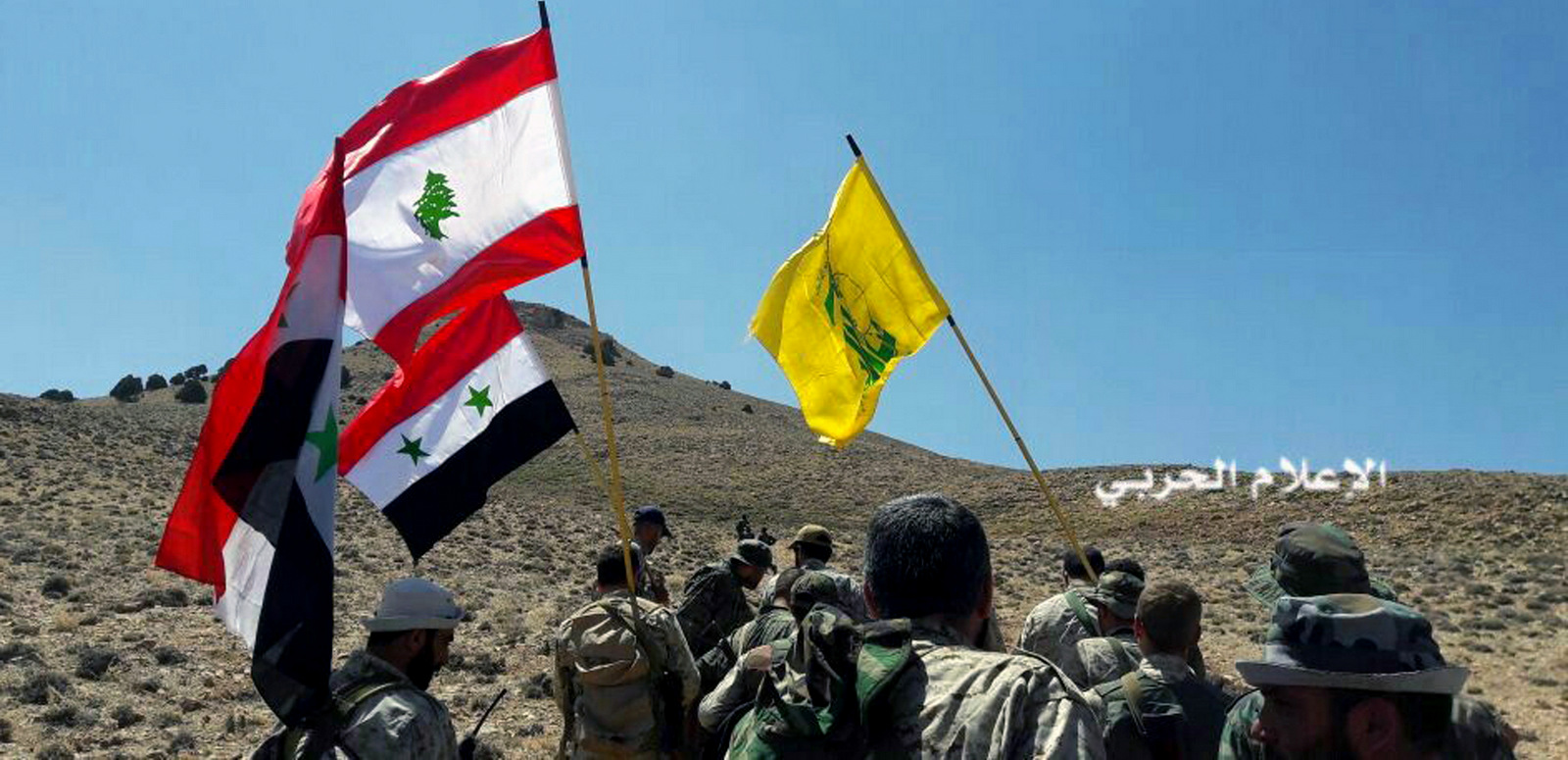 Hezbollah fighters advancing up a hill as they hold Lebanese, Syrian and their group's flags in the mountainous region of Qalamoun, Syria, Aug 28, 2017. (Syrian Central Military Media, via AP)