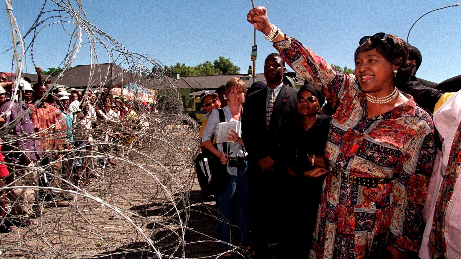 Madikizela-Mandela greets demonstrators, behind razor wire at a bail hearing for businessman Piet Odendaal in Viljoenskroon, in the Orange Free State, South Africa, Nov. 10, 2000. (AP/Lori Waselchuk)