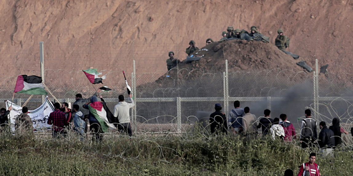 Protesters wave Palestinians flags in front of Israeli solders on Gaza's border with Israel, east of Beit Lahiya, Gaza Strip, Wednesday, April 4, 2018. A leading Israel human rights group urged Israeli forces in a rare step Wednesday to disobey open-fire orders unless Gaza protesters pose an imminent threat to soldiers' lives. (AP Photo/Adel Hana)
