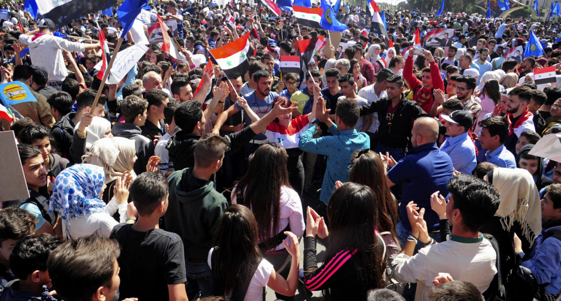 Syrians wave flags and portraits of President Bashar Assad during a demonstration to show solidarity with the Syrian armed forces, at Omayyad Square, in Damascus, Syria, April 16, 2018. Syrians gathered in a landmark square in the capital of Damascus in support of their armed forces, which they say succeeded in confronting the unprecedented joint airstrikes by the West over the weekend. (SANA via AP)