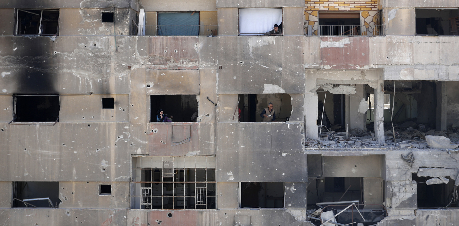 In this Monday, April 16, 2018 photo, people look out of their damage apartment windows just meters away from where the alleged chemical weapons attack occurred in the town of Douma, the site of a suspected chemical weapons attack, near Damascus, Syria. The survivors blamed the attack on the Army of Islam, the powerful rebel group that controlled the town before it was taken over by Syrian government forces this week, although they did not offer evidence to back up their claims.(AP/Hassan Ammar)