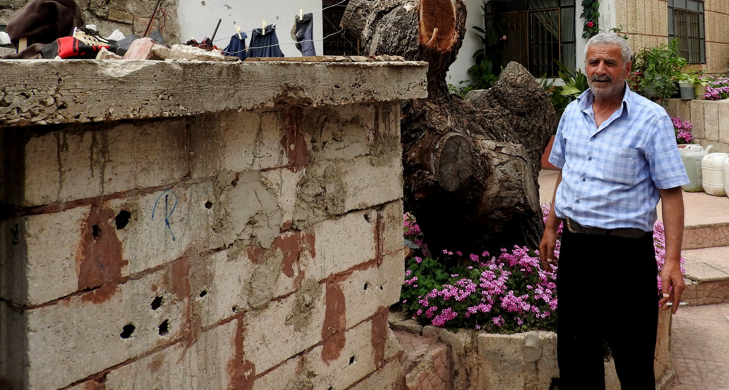 A Hadar resident stands outside of his shrapnel damaged home. Eva Bartlett | MintPress News