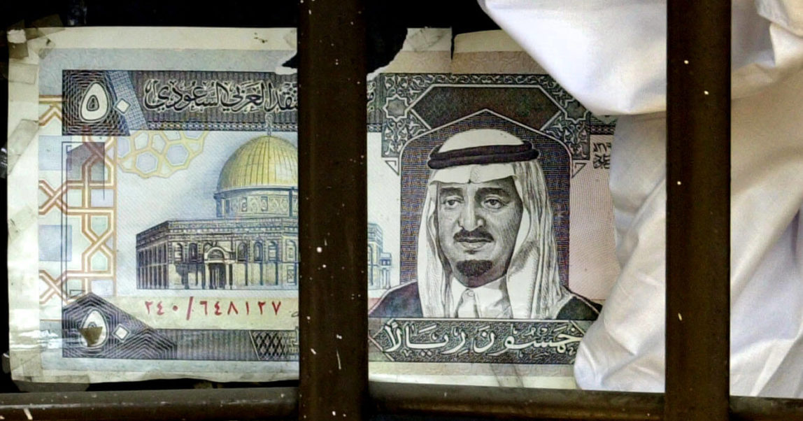 A money exchanger sits next to mock a Saudi rial featuring a depiction of Jerusalem rial bill advertising his business at a bazaar in the southwest Pakistan. Enric Marti | AP