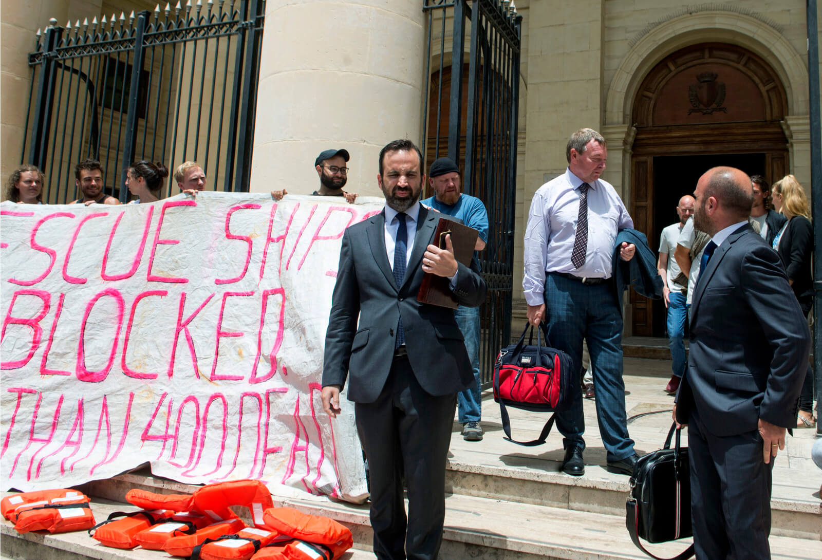 Claus-Peter Reisch, second from right, captain of Lifeline rescues ship, stops next to members of his crew staging a protest as he leaves after an arraignment hearing in Valletta, Malta, July 2, 2018. str | AP