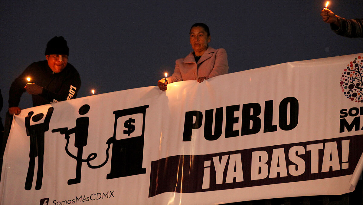 Protesters hold candles by a sign that reads in Spanish "Enough already!" outside the headquarters of the government-run PEMEX oil company in Mexico City, Sunday, Jan. 8, 2017. People are protesting a 20-percent gasoline price hike after the government stopped subsidizing and regulating prices for gasoline and diesel. (AP Photo/Marco Ugarte)
