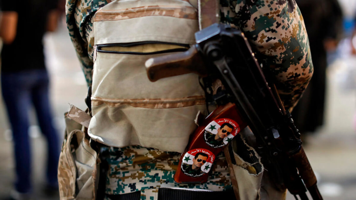 A Syrian army soldier holds his AK-47 rifle with stickers showing President Bashar Assad and Arabic that reads, "Heroes of Assad's Syria," as he stands guard at a check point at the Hamadiyah market, named after the 34th Sultan of the Ottoman Empire Abdul Hamid II, in the Old City of Damascus, Syria, July 19, 2018. Hassan Ammar | AP