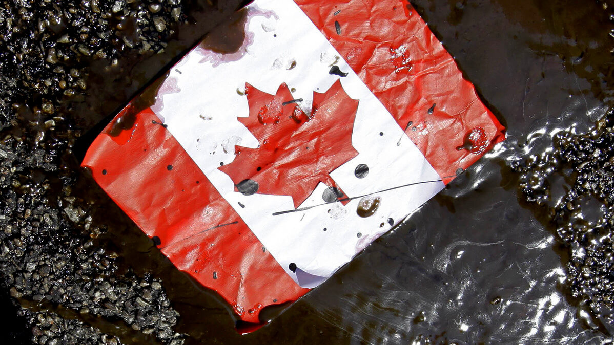 A placard with the Canadian flag rests on the ground covered in oil as demonstrators protest against the Keystone XL Pipeline and the Alberta tar sands.