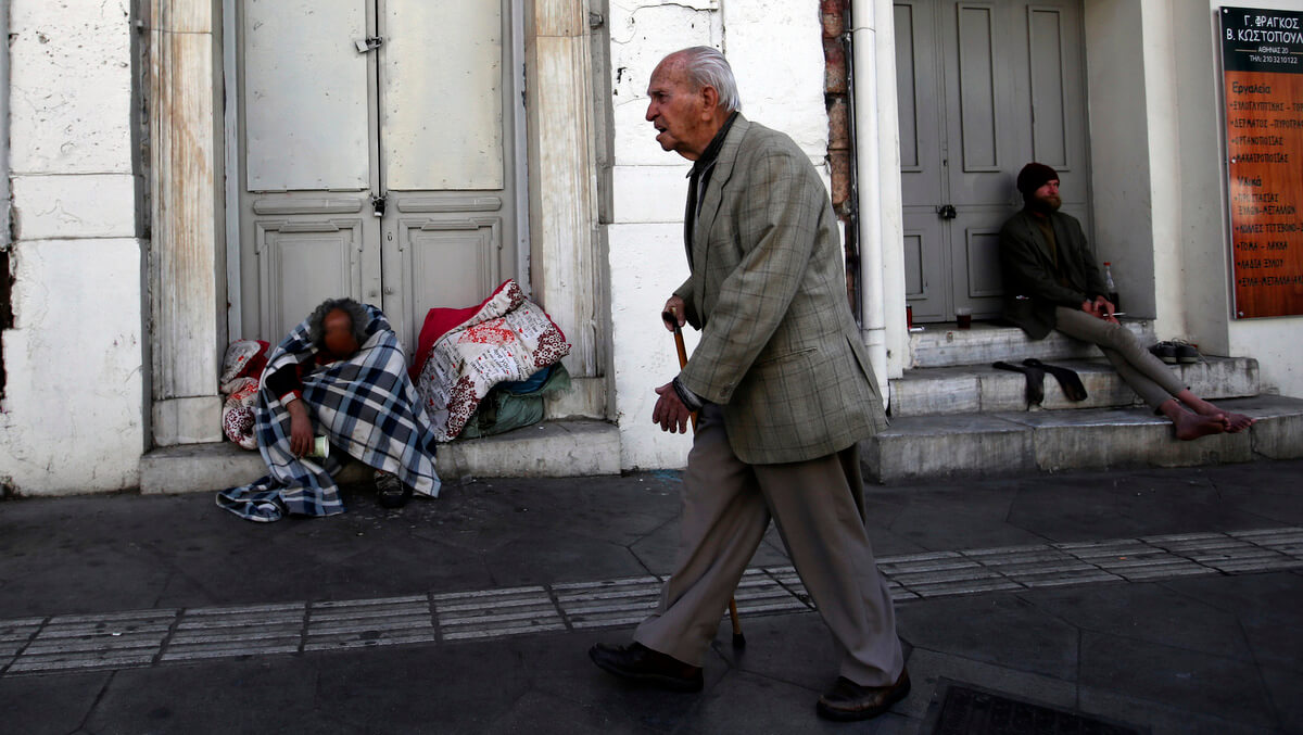 An elderly man passes by homeless men in Athens, April 23, 2018. Thanassis Stavrakis | AP
