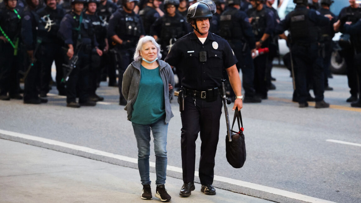 Police officer arrests protester during Los Angeles anti-ICE protest as riot police stand in formation