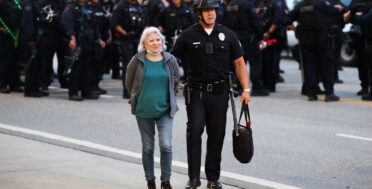 Police officer arrests protester during Los Angeles anti-ICE protest as riot police stand in formation